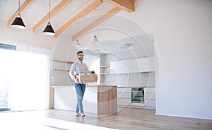 Mature man walking in unfurnished house, holding a moving box.