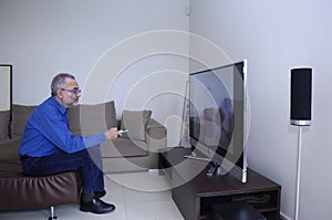 Mature Man Watching Television And Using Remote Control