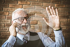 Mature man waving while talking on mobile phone.