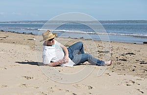 Mature man wearing a hat and sunglasses resting on the beach in summer.