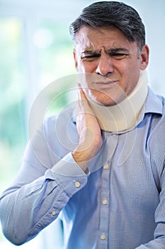 Mature Man Wearing Neck Brace Winces With Pain