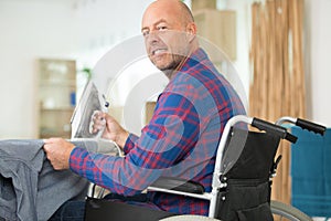 Mature man in wheelchair ironing shirt