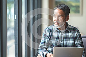 Mature man with white stylish short beard looking outside window. Casual lifestyle of retired hispanic people