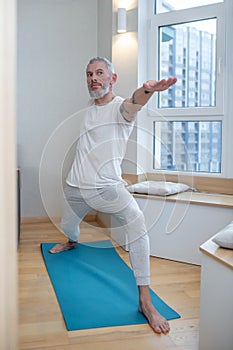 A mature man in a white tsirt standing in a warrior pose