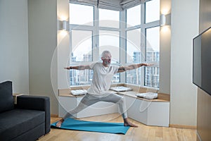 A mature man in a white tsirt standing in a warrior pose