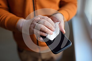 Mature man wipes with a disinfecting cloth heis smartphone after returning home. Safety during COVID-19 outbreak in public places