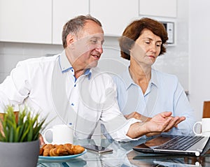 Mature man and woman talking while working at laptop together at home