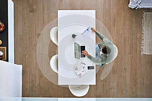 Mature man working on laptop sitting at kitchen home table, top view.