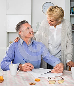 Mature married couple discuss contract and sign important docum