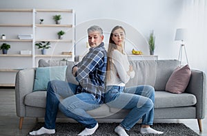 Mature married man and his wife sitting back to back on sofa, not knowing how to make peace after conflict