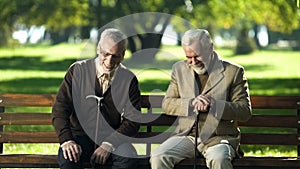 Mature men with walking sticks sitting bench in park laughing talking about life