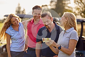 Mature And Mid Adult Couples Standing By Golf Buggy Checking Score Cards Together