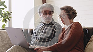 Mature mid age couple using laptop sit on sofa. White hair. New technology for older people.