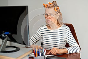 Mature middle aged in glasses using laptop typing email working at home office, lady searching information on internet