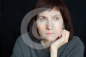 Mature, middle-aged woman looks anxiously ahead, chin propped on hand. Close-up portrait