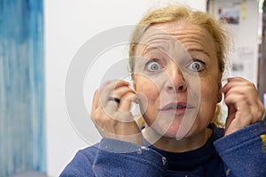 Mature, middle aged woman looks desperate with eyes wide open beats her ears with her hands, copy space