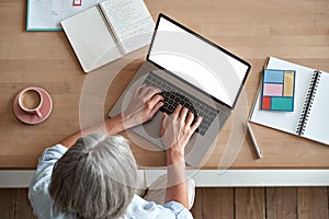 Mature middle aged woman using laptop computer sitting at workplace, top view.