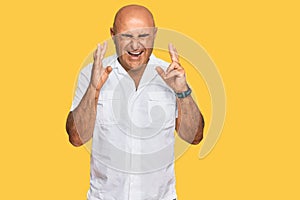 Mature middle east man with mustache wearing casual white shirt gesturing finger crossed smiling with hope and eyes closed