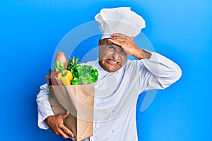 Mature middle east man professional chef holding bag of groceries stressed and frustrated with hand on head, surprised and angry
