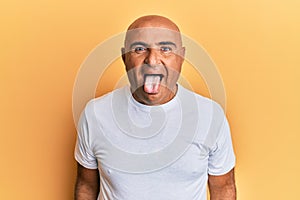 Mature middle east man wearing casual white tshirt sticking tongue out happy with funny expression