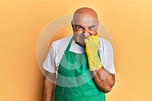 Mature middle east man wearing cleaner apron and gloves looking stressed and nervous with hands on mouth biting nails