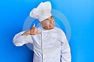 Mature middle east man wearing professional cook uniform and hat smiling doing phone gesture with hand and fingers like talking on