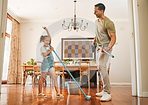 Mature mixed race dad and his young little daughter pretending to play the guitar by using a broom in a lounge at home