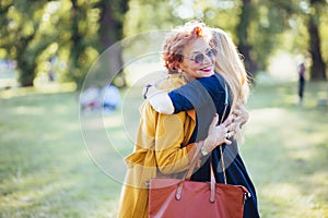 Mature mother and adult daughter hugging in the park