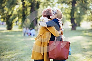 Mature mother and adult daughter hugging in the park