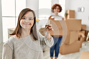 Mature mother and down syndrome daughter moving to a new home, standing by cardboard boxes showing house key chain