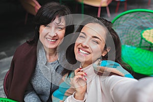 Mature mother and her young daughter sit together in cafe or restaurant. Cheerful positive happy women posing on camera