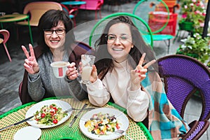 Mature mother and her young daughter sit together in cafe or restaurant. Posing on camera and smil during lunchtime