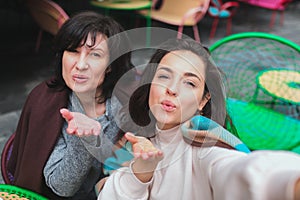 Mature mother and her young daughter sit together in cafe or restaurant. Selfie or beautiful women different ages