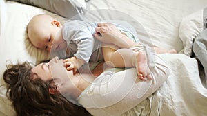 Mature mother plays with the baby lying in bed. The kid touches his finger to the mouth of the mother, the development