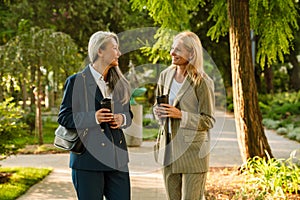 Mature multiracial businesswomen drinking coffee during walking in park