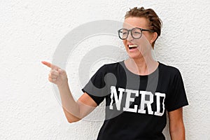 Mature nerd woman wearing big eyeglasses and standing against white background outdoors while laughing and pointing