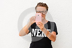Mature nerd woman wearing big eyeglasses and standing against white background outdoors while photographing with mobile