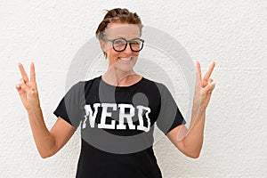 Mature nerd woman wearing big eyeglasses and standing against white background outdoors while smiling and making peace