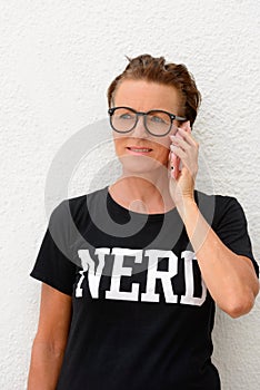 Mature nerd woman wearing big eyeglasses and standing against white background outdoors while talking on mobile phone