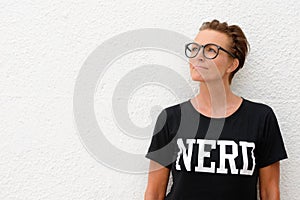 Mature nerd woman wearing big eyeglasses and standing against white background outdoors while thinking and looking up