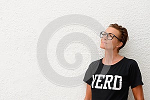 Mature nerd woman wearing big eyeglasses and standing against white background outdoors while thinking and looking up to