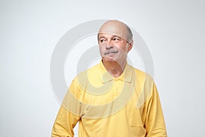 Mature old attractive man in yellow shirt with skeptic look, raises eyebrow in bewilderment, has some doubts