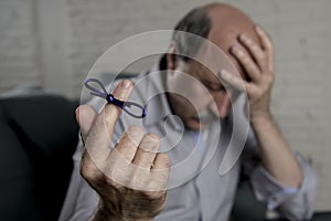 Mature old man on his 60s at home couch alone feeling sad and worried suffering alzheimer disease holding ribbon