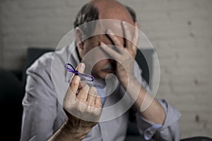 Mature old man on his 60s at home couch alone feeling sad and worried suffering alzheimer disease holding ribbon