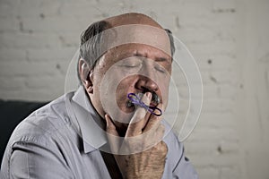 Mature old man on his 60s at home couch alone feeling sad and worried suffering alzheimer disease holding ribbon