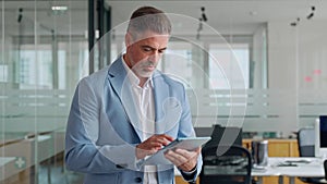 Mature older business man executive using digital tablet standing in office.