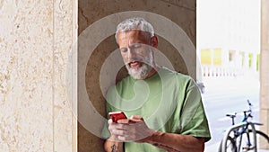 Mature older middle aged man using smartphone standing on the street outdoors.