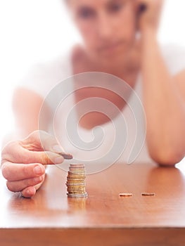 Mature older woman putting coins into a pile, heap, on table. Defocussed high key background. Poverty concept, counting