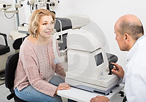 Mature optician examinating eyesight with aid of slit lamp