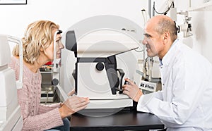 Mature optician examinating eyesight with aid of slit lamp